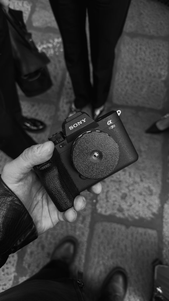 A Sony camera held in a gloved hand, black and white
