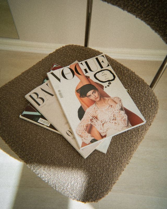 A stack of fashion magazines on a boucle chair in afternoon light